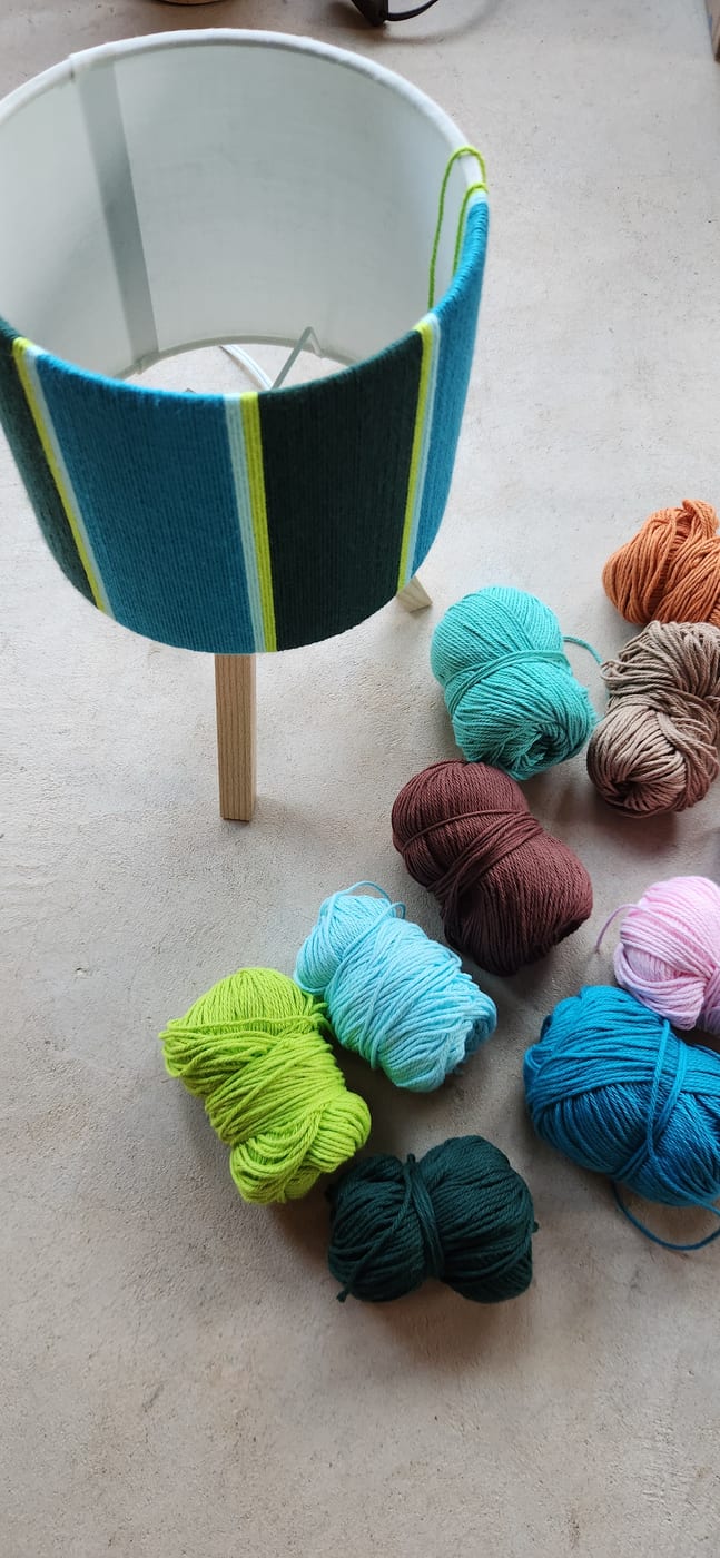A finished teal and lime wrapped lamp beside the leftover balls of yarn