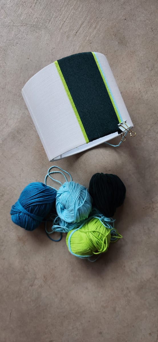 A shade half wrapped in dark green and lime yarn, clipped in place