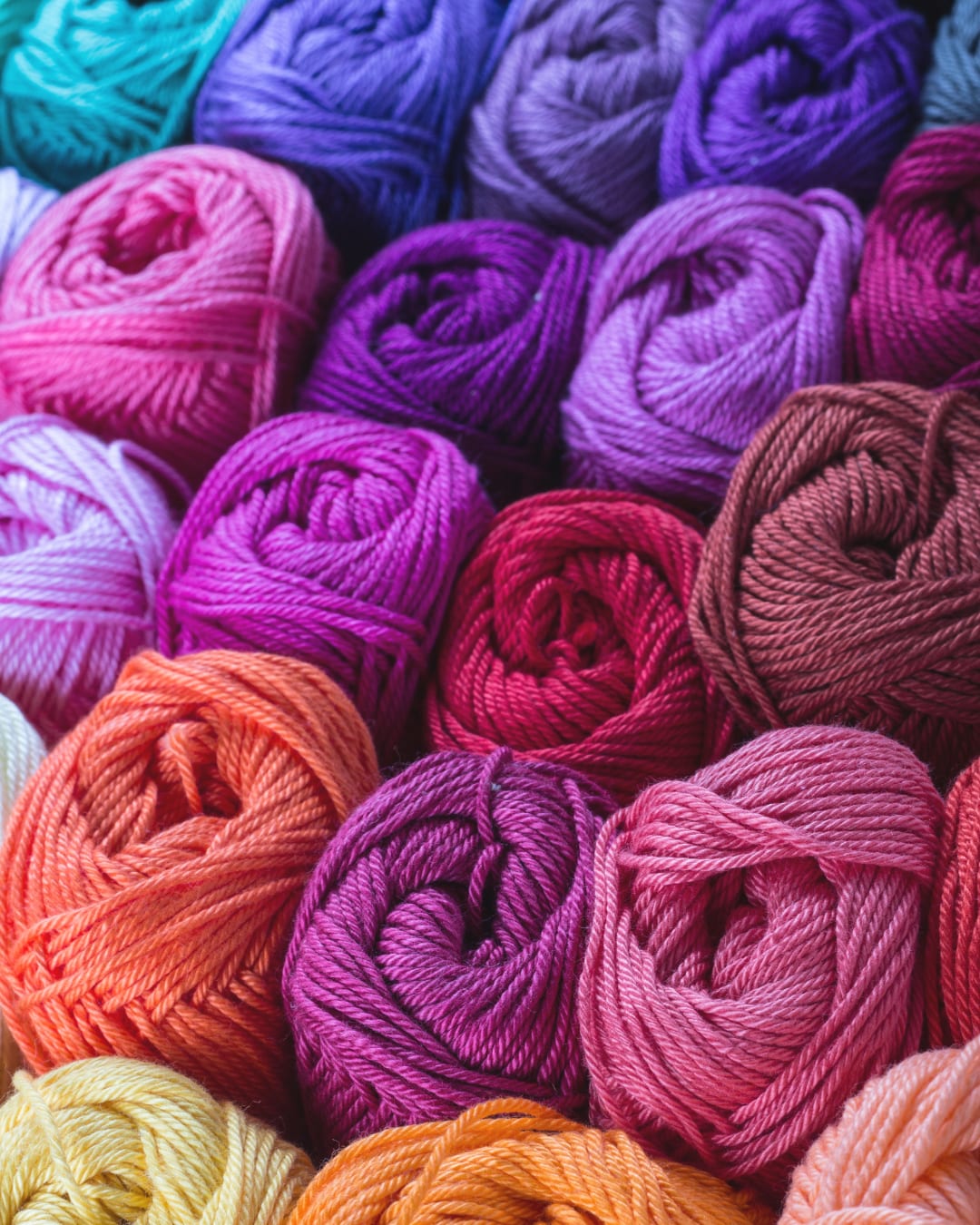 Balls of yarn in pinks, purples and oranges packed tightly together