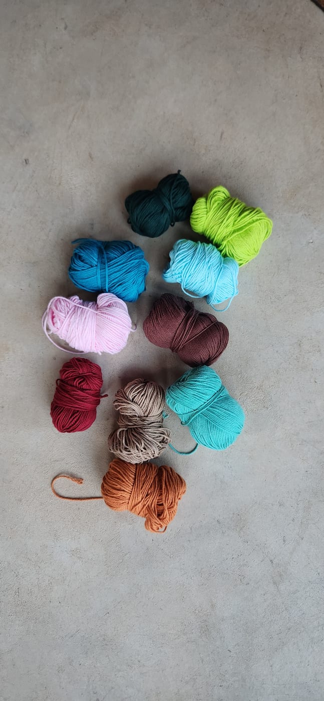 Balls of yarn in rust, teal and sand laid out on a concrete floor